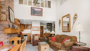 A cozy living room with a fireplace, wooden furniture, and a staircase leading to an upper level.