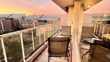 Enjoy the city view from this balcony with a table, chairs, and a potted plant.