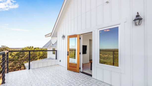 A white building with a balcony, a wooden door, and a window overlooking a landscape. - Hilltop Views, Dog Friendly, Deck, Fire Pit & Near Pedernales Falls (Johnson City)