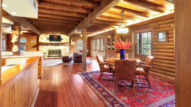 A log cabin interior with a wooden dining area, fireplace, and large windows. - Mill Race Lodge I Waterfront, Pool, Wimberley (Wimberley)
