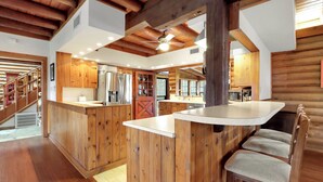 A spacious kitchen with wooden cabinetry, a central island, and a bar area with seating. - Mill Race Lodge I Waterfront, Pool, Wimberley (Wimberley)