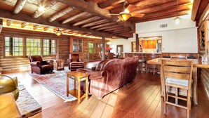 A spacious log cabin interior with a wooden ceiling, leather sofas, and a dining area. - Mill Race Lodge I Waterfront, Pool, Wimberley (Wimberley)