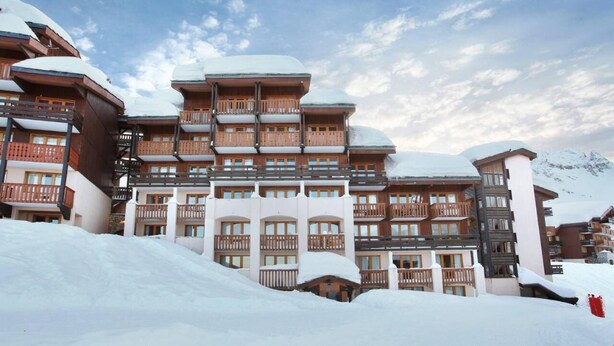 Un hôtel à plusieurs étages, doté de balcons et de toits enneigés, qui se dresse sur fond de montagnes.