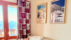 Un salon chaleureux avec un canapé beige, des rideaux à motifs et deux tableaux encadrés représentant des scènes hivernales.