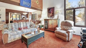 Een ruime woonkamer met een bank, fauteuil en salontafel. Een groot raam biedt uitzicht op het omliggende landschap.