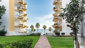 Un camino que lleva a un edificio con varios balcones, palmeras y vista al mar.