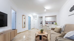 Una sala de estar moderna con un televisor, una mesa redonda de centro, un sofá y una cocina al fondo.