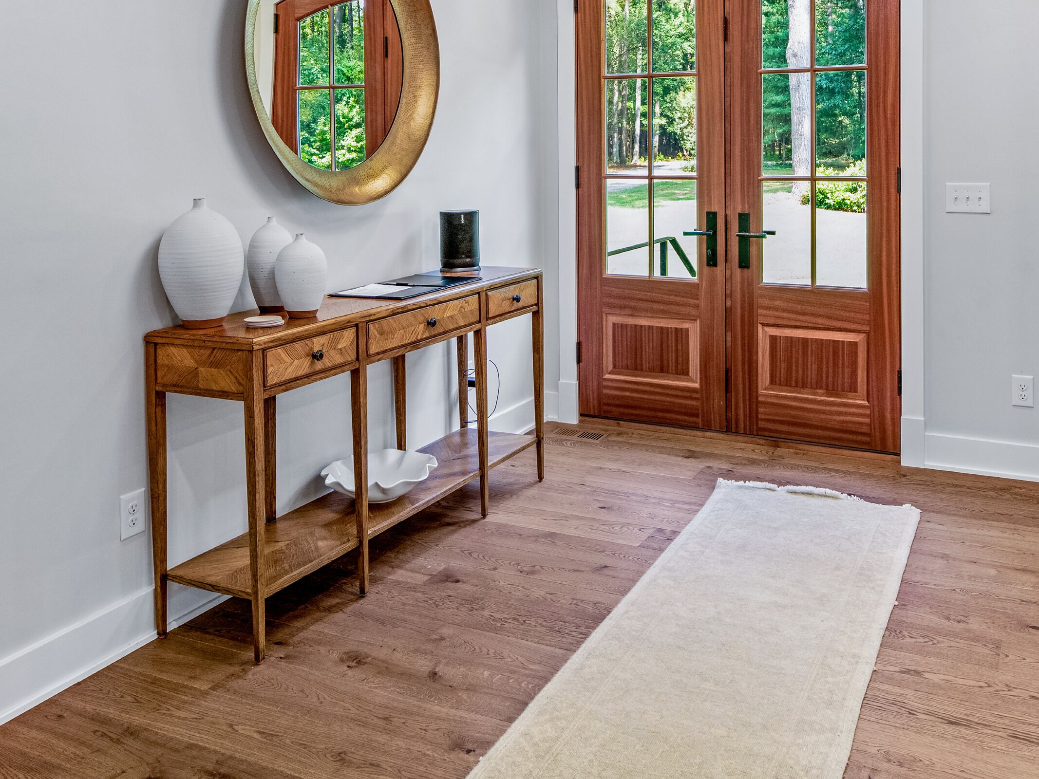 A wooden console table with vases, a black tray, and a mirror.