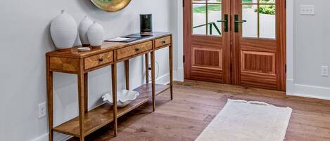 A wooden console table with vases, a black tray, and a mirror.