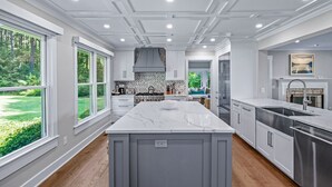 Een moderne keuken met een groot eiland, witte kasten en uitzicht op een groen landschap door grote ramen.