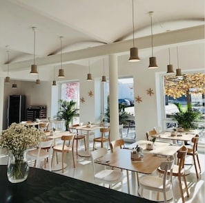 Un comedor moderno con varias mesas y sillas, iluminación colgante y grandes ventanales con vistas al exterior.
