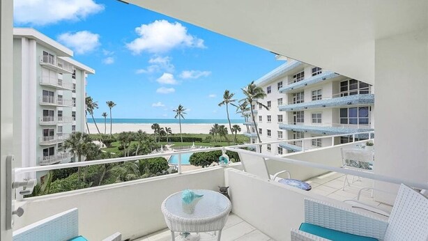 A balcony with a view of a beach, palm trees, and a pool.