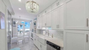 A modern kitchen with white cabinetry, a dishwasher, and a dining area with white chairs and a blue table.