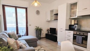 Een moderne woonkamer met een grijze bank, een eettafel en een keuken met een magnetron, oven en kasten.