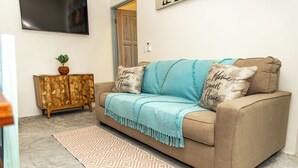 A living room with a beige sofa, two throw pillows, a patterned rug, a wooden cabinet, and a flat-screen TV on the wall. - Babylon Beach Villa 8    (San Pedro)