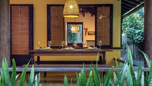 A dining area with a wooden table set for four, surrounded by large green plants.