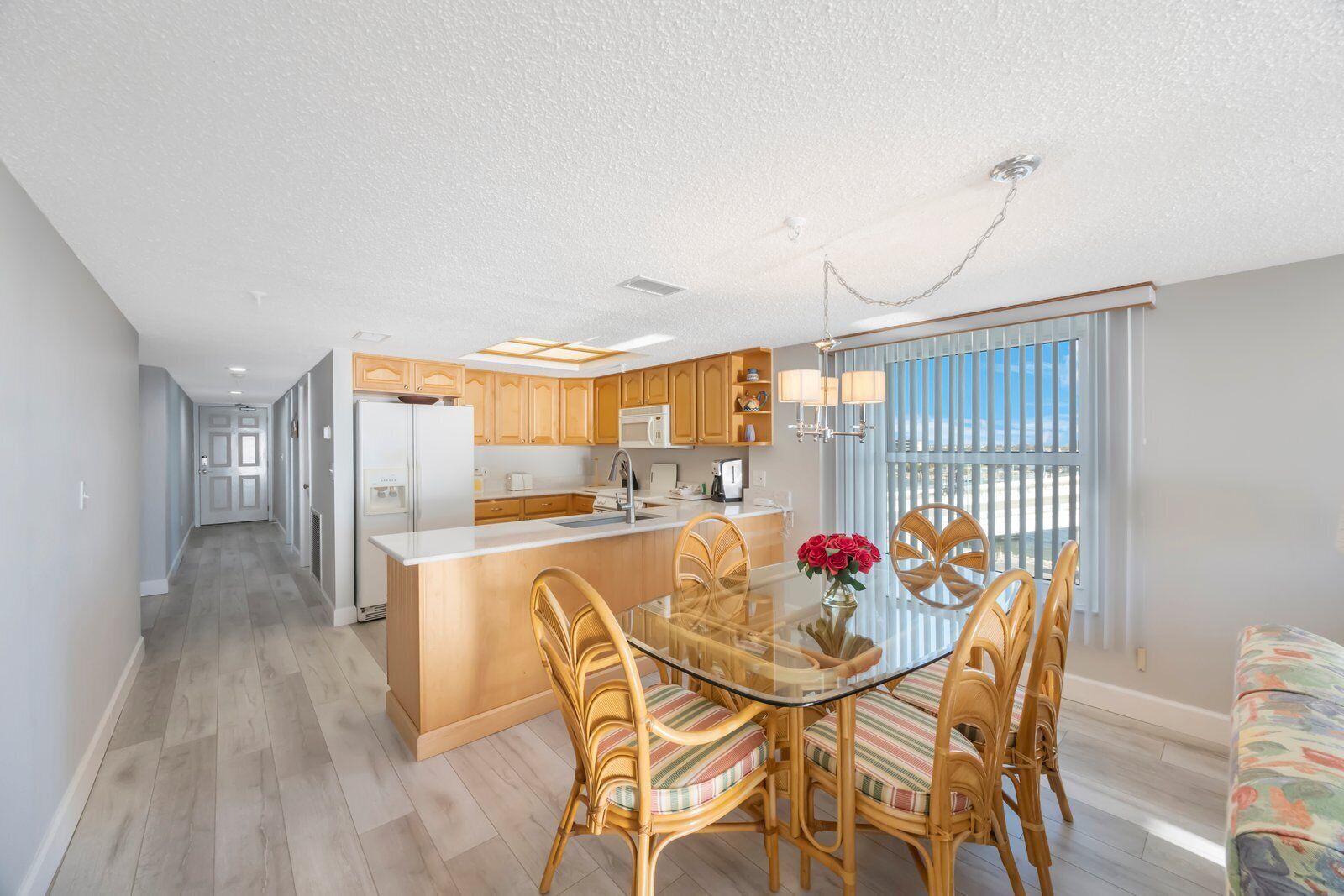 A modern kitchen with wooden cabinets, a central island, and a dining area with wicker chairs and a glass table.