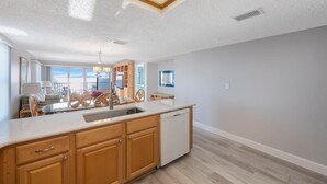 A modern kitchen with wooden cabinets, a dishwasher, and a large window overlooking a balcony.