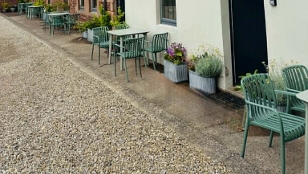 Een rij witte gebouwen met een bord waarop staat 'Town Farm Cottages'. Er zijn buiten zitplekken met groene stoelen en potplanten.