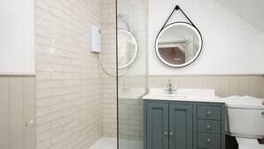 Een badkamer met een douchecabine van glas, een wit wastafelmeubel, toilet en een kast met lades.