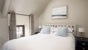Een slaapkamer met een groot bed, een nachtkastje met een lamp, een raam met gordijnen en een schilderij aan de muur.