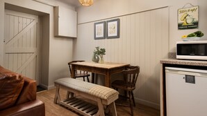Een kleine keuken met een houten tafel, een bankje en stoelen, een magnetron en een koelkast.