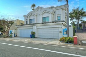 A two-story house with a garage, a driveway, and a small garden with plants and a palm tree.