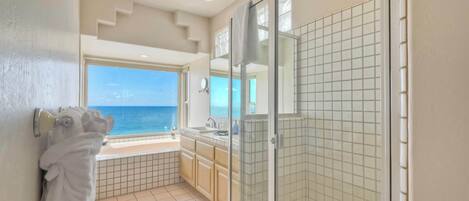 Un baño con ducha de vidrio, lavamanos y un amplio ventanal con vista al océano.