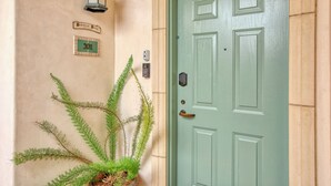 A green door with a number plate, a potted fern, and a wall-mounted light fixture. - Ocean-View Luxury at Valentina Suites - Suite 201 (Pismo Beach)