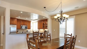 A spacious kitchen with wooden cabinets, a stainless steel refrigerator, a microwave, and a dining table with chairs. - Ocean-View Luxury at Valentina Suites - Suite 201 (Pismo Beach)