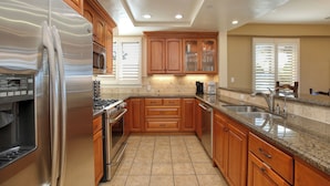 A kitchen with wooden cabinets, stainless steel appliances, and a granite countertop. - Ocean-View Luxury at Valentina Suites - Suite 201 (Pismo Beach)