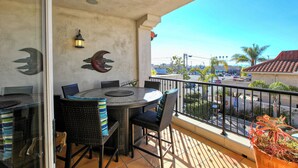 A balcony with a round table and chairs, a potted plant, and a view of the street.