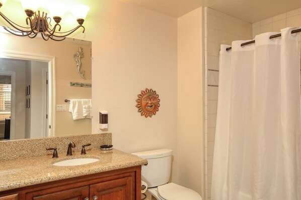 A bathroom with a granite countertop sink, a wooden vanity, a toilet, and a shower curtain.