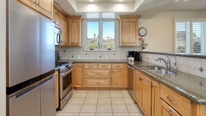 Una cocina con armarios de madera, electrodomésticos de acero inoxidable, un ventanal y vistas al exterior.
