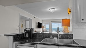 A modern kitchen with a Bosch dishwasher, a coffee maker, and a large window overlooking the ocean. - Birds' Nest -oceanfront condo in Dunescape Villas with beautiful views (Atlantic Beach)