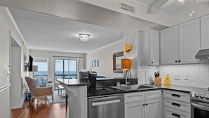 A modern kitchen with white cabinets, stainless steel appliances, and a view to the outside. - Birds' Nest -oceanfront condo in Dunescape Villas with beautiful views (Atlantic Beach)