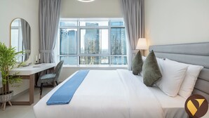 Une chambre d’hôtel avec un grand lit, un bureau, une chaise, un miroir et une vue sur de hauts immeubles par la fenêtre.