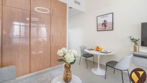 Une chambre d’hôtel moderne avec une armoire en bois, un coin repas comprenant deux chaises et une table, un vase avec des fleurs et un tableau encadré au mur.