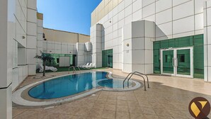 Un espace piscine intérieure moderne, doté d’une piscine à l’eau d’un bleu limpide, de chaises longues et d’une entrée avec une porte en verre.