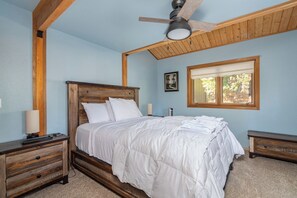 Ein Schlafzimmer mit Holz Kopfteil, einem Einzelbett, einem Nachttisch, einer Lampe, einem Fenster mit Aussicht und einem Deckenventilator.