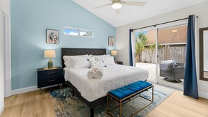 Un dormitorio con cama, mesitas de noche, ventilador de techo y vistas al exterior.