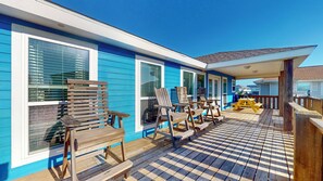 Un edificio blu con un patio a scacchi, sedie di legno e una zona coperta con un tavolo.