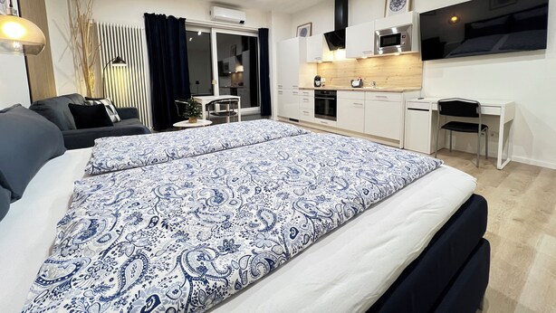 A modern bedroom with a large bed, a small desk, and a kitchenette. - Marketplace atrium 1 on the ground floor (Höxter)