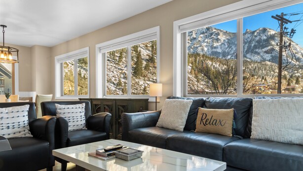 Un salon comprenant un canapé, des fauteuils, une table basse et offrant une vue sur des montagnes enneigées grâce à de grandes fenêtres.