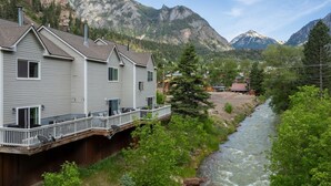 Une maison dotée d’une terrasse donnant sur une rivière, entourée de montagnes.
