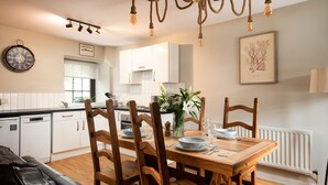 A dining area with a wooden table, chairs, and a clock on the wall. - Two bedroom Cottage in the heart of Beadnell (Beadnell)