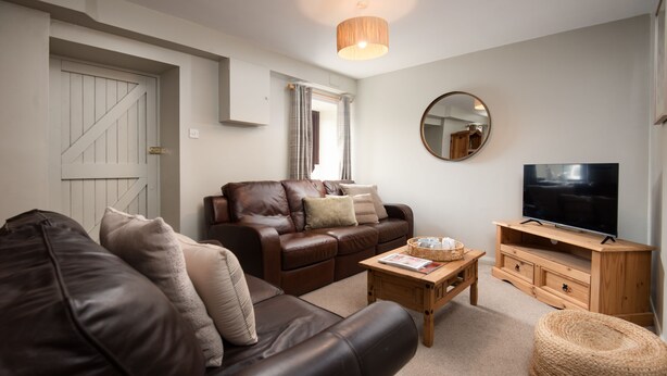 A living room with a sofa, a coffee table, a television, and a mirror. - Two bedroom Cottage in the heart of Beadnell (Beadnell)