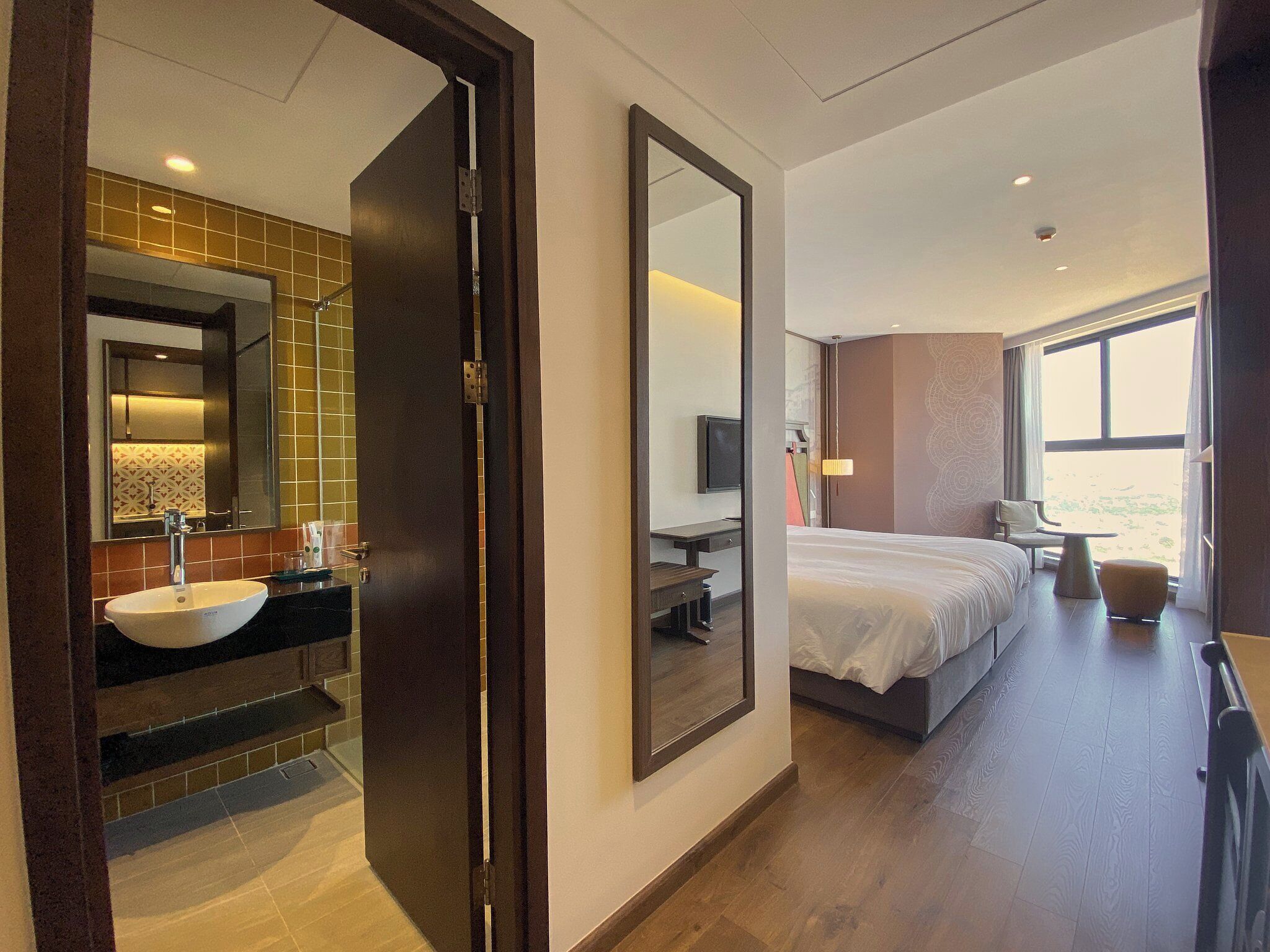 Ein Hotelzimmer mit einem großen Bett, einem Schreibtisch, einem Stuhl, einem Fernseher und einem Badezimmer mit Waschbecken und Spiegel.