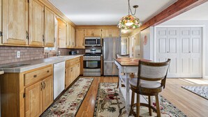 A kitchen with wooden cabinets, stainless steel appliances, a central island, and a hanging light fixture. - 5 Bedroom Beach Retreat (Narragansett)