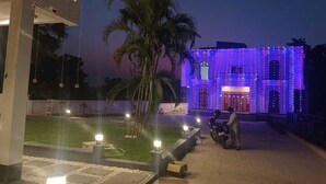 A building with a well-lit entrance and a paved area with a palm tree and a motorcycle parked nearby. - Rani Kutir Resort (Bolpur)